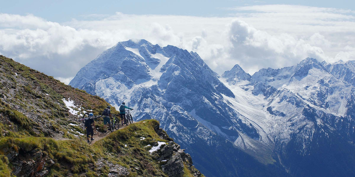 Eine Gruppe mit Fahrrädern auf einem Bergweg vor weitem Alpenpanorama