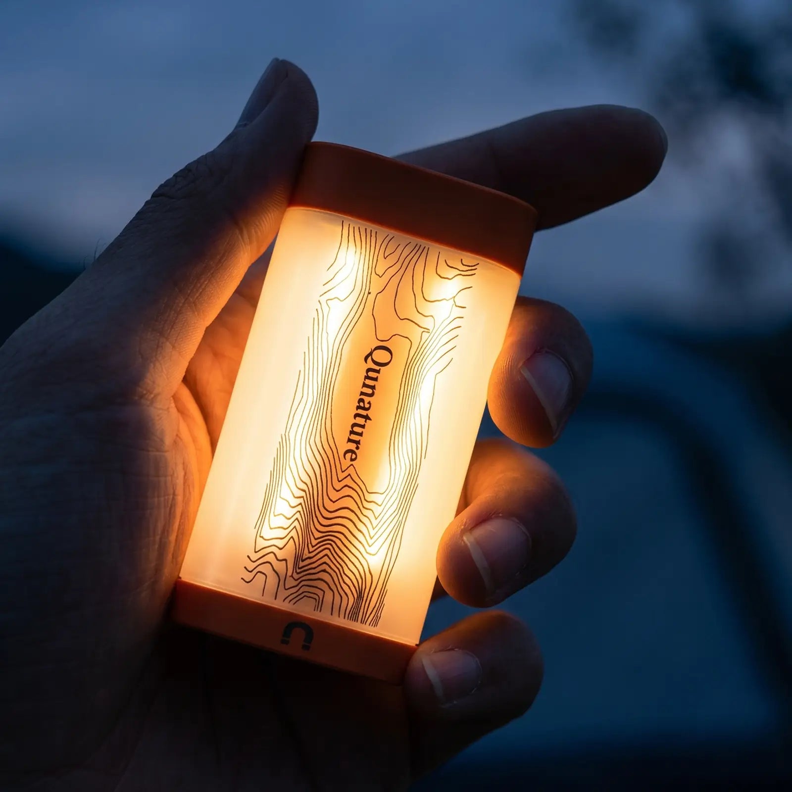 hand hält kleine orange campinglampe mit topografie muster warmes licht im dämmerlicht