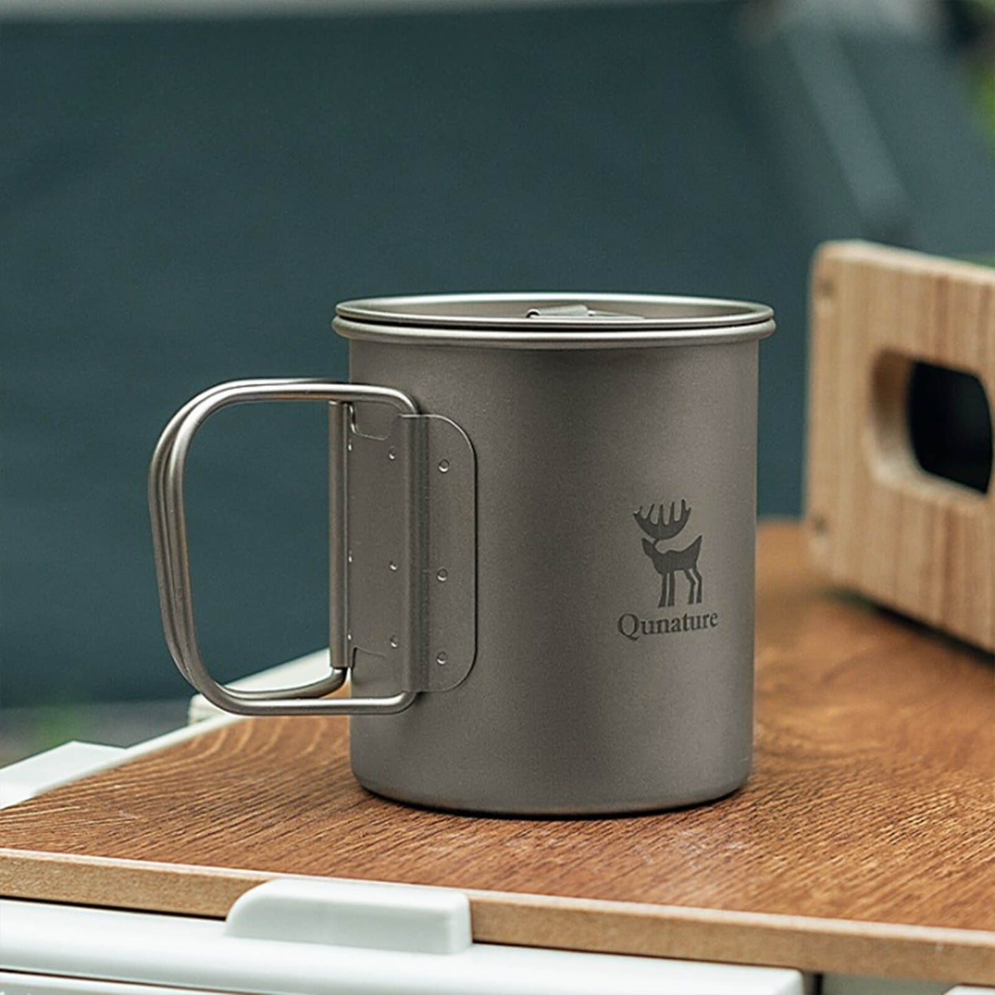 titan camping cup with lid and foldable handle, placed on a wooden camping table