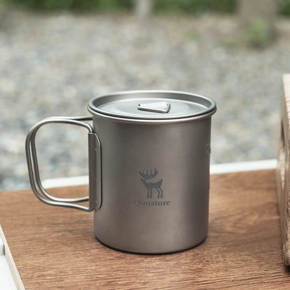 close-up of a pure titanium camping cup with foldable handle and lid on a wooden table