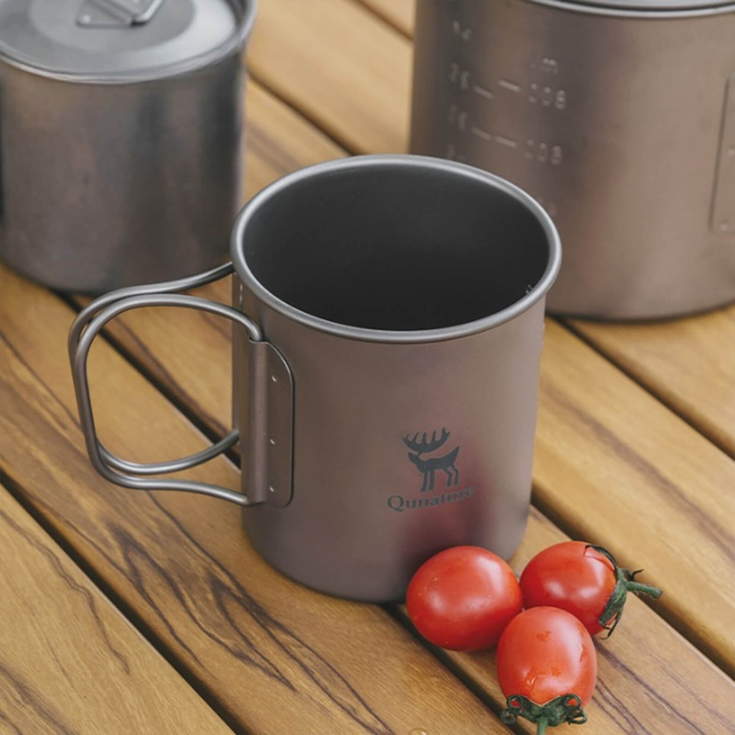 open titanium camping cup with foldable handle, on wooden picnic table with cherry tomatoes